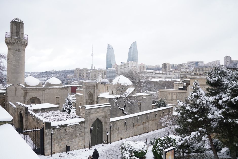 A snowy landscape of Baku featuring the historic Old City and modern Flame Towers in the b