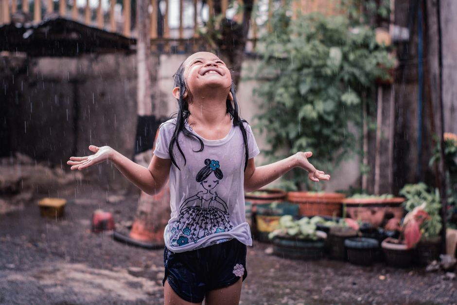 Happy child enjoying playing in the rain, wearing a white t-shirt and shorts. Captured outdoors.