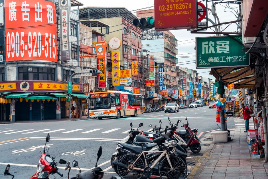 Vibrant Taiwanese city street bustling with scooters, buses, and colorful signage.