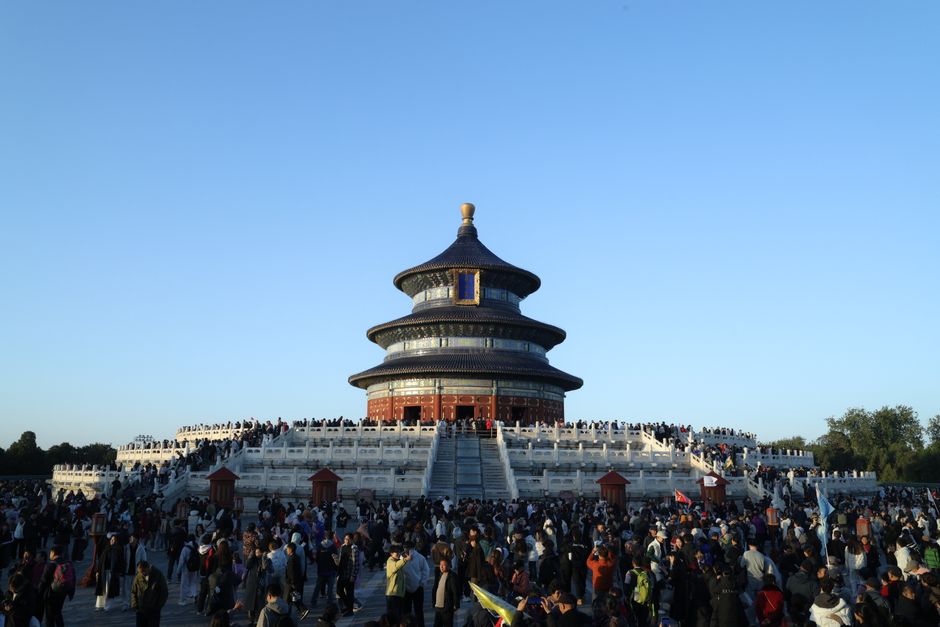 Large crowd gathered at the iconic Temple of Heaven in Beijing, China, under a clear blue sky.