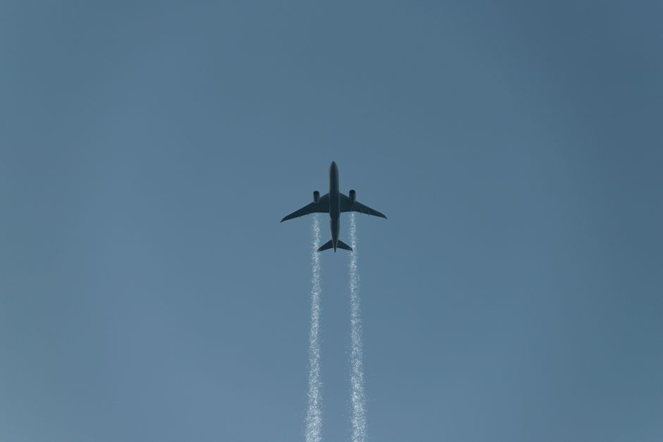 A commercial airplane leaving contrails as it flies across a clear blue sky, viewed from below.