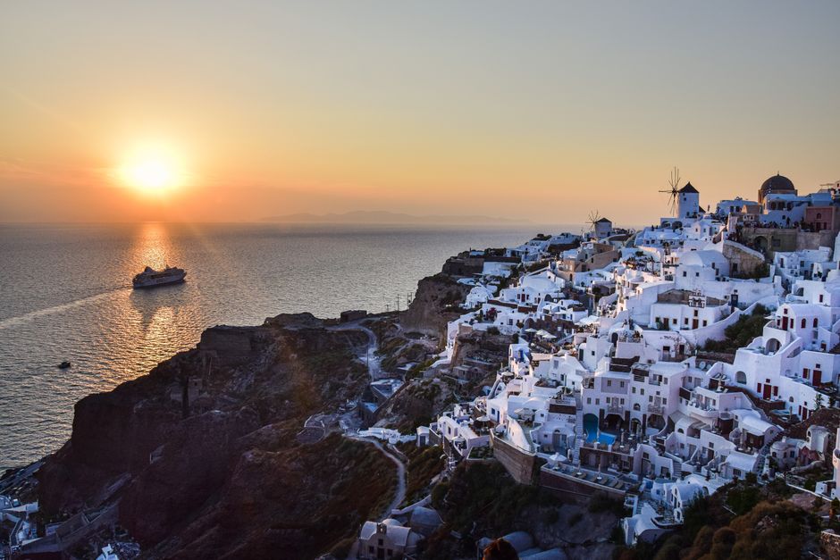 Beautiful sunset view of Santorini's whitewashed buildings and a cruise ship in the Aegean Sea.