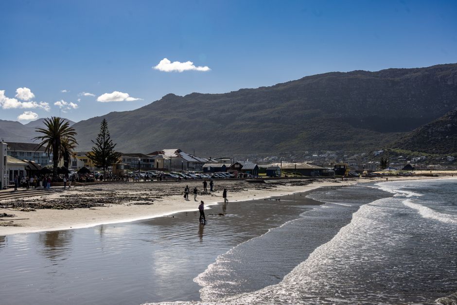 Beautiful coastal landscape with mountains, beachgoers, and ocean waves under clear skies.