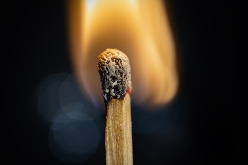 Macro shot of a burning matchstick with vibrant flame and textured match head.