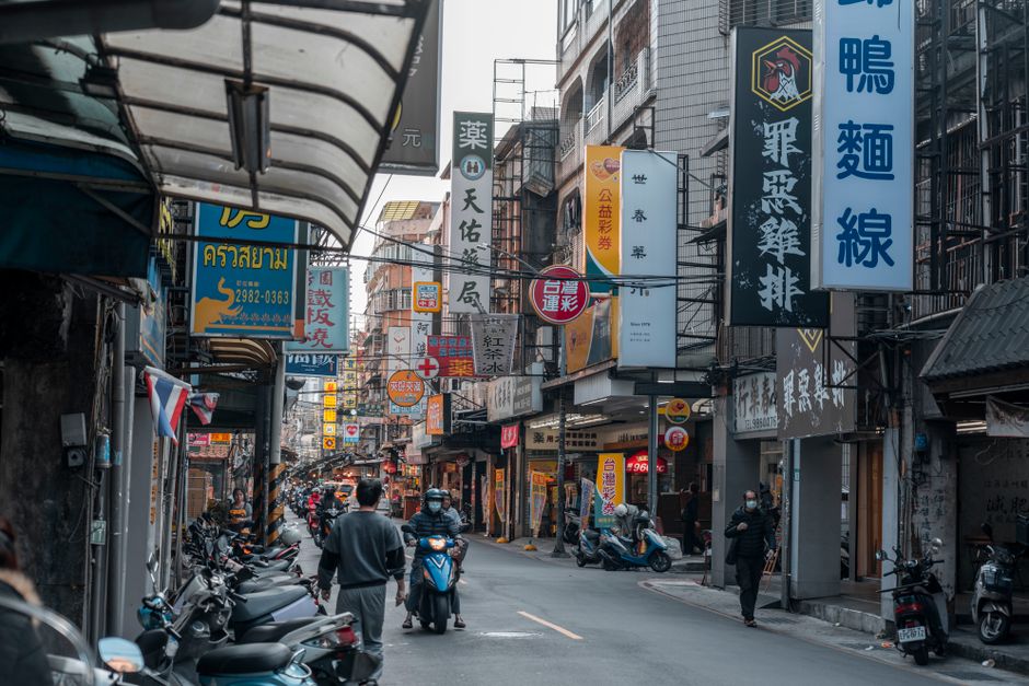 Lively street in an Asian city featuring motorbikes and vibrant storefront signs.