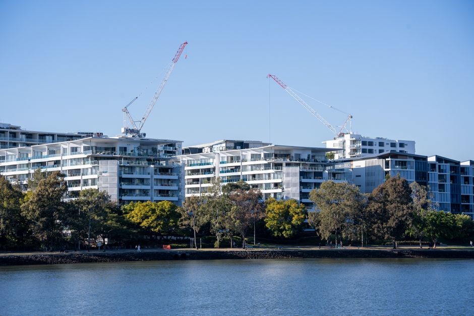 Luxurious riverside apartments under construction with cranes against a clear blue sky.