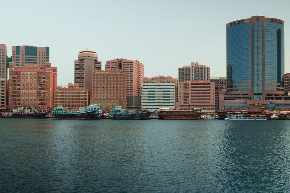 A modern skyline in Dubai with waterfront and traditional boats.