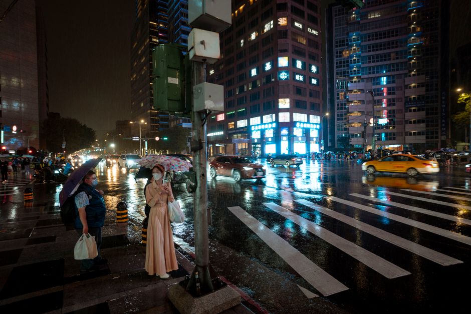 Nighttime city scene with pedestrians using umbrellas and face masks in the rain.