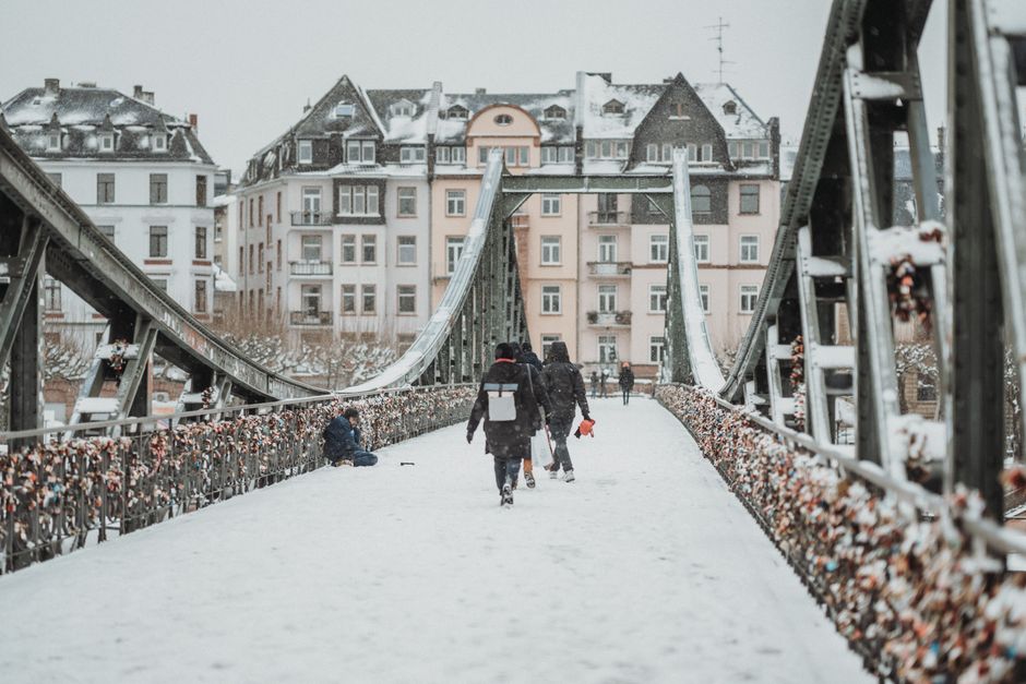 Pedestrians walking on a snow-covered iron footbridge in a historic European city during w