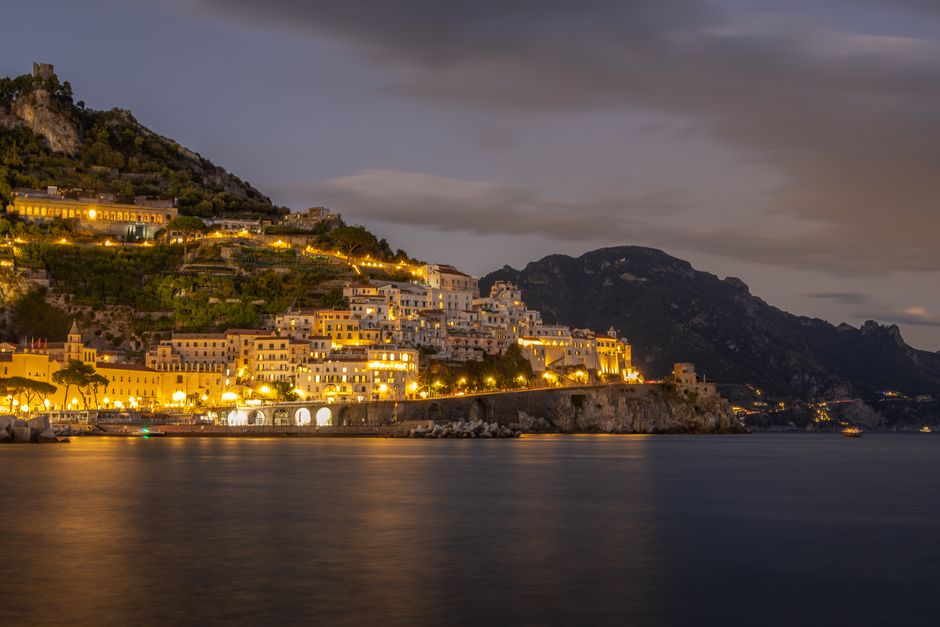 Stunning twilight view of the illuminated Amalfi Coast, Italy with calm waters.