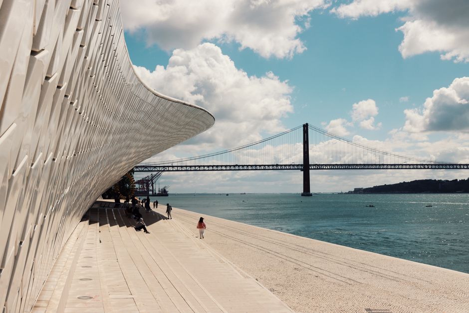 An urban landscape featuring the iconic 25 de Abril Bridge and MAAT in Lisbon, Portugal.