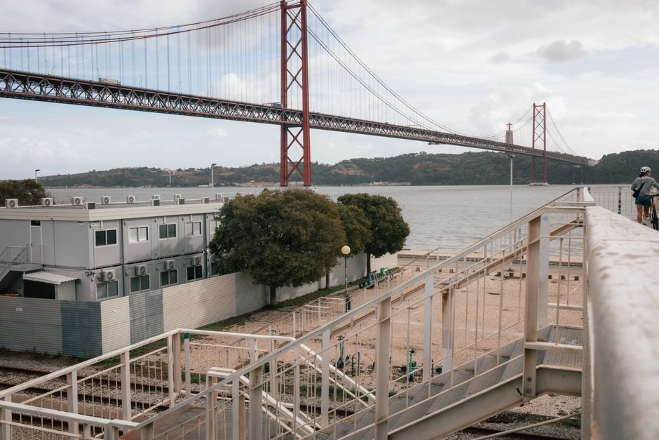 View of a large suspension bridge over a river, with a cityscape and cyclists in the foreground.