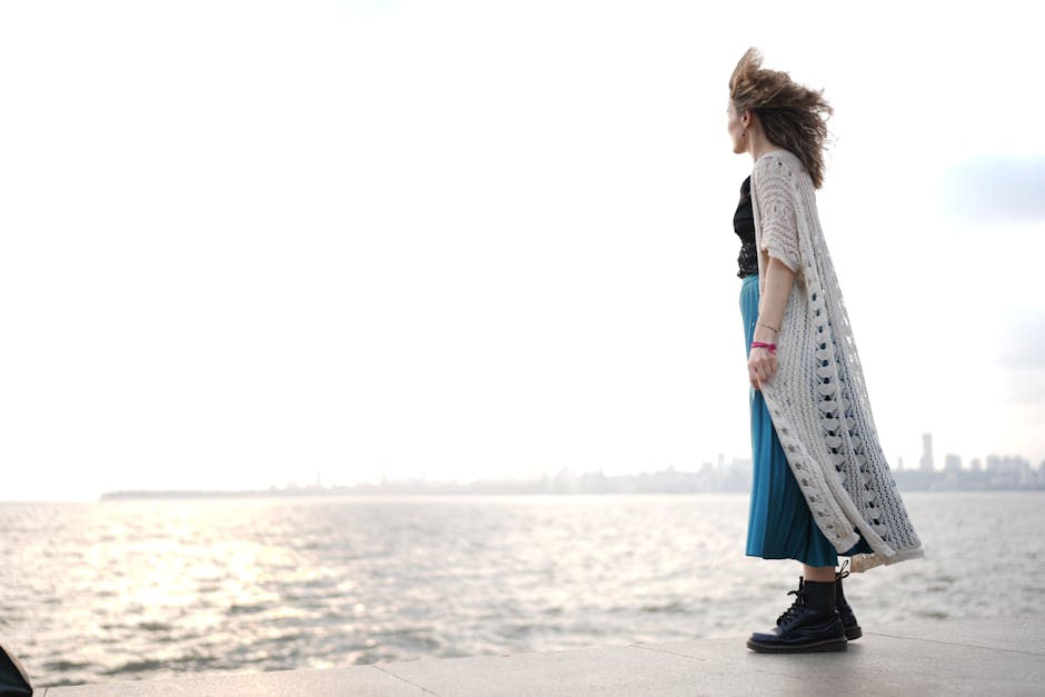 Young woman gazing at the ocean with city skyline in the distance, embracing freedom.