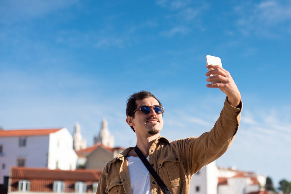 Confident man wearing sunglasses capturing a selfie with clear blue sky background.