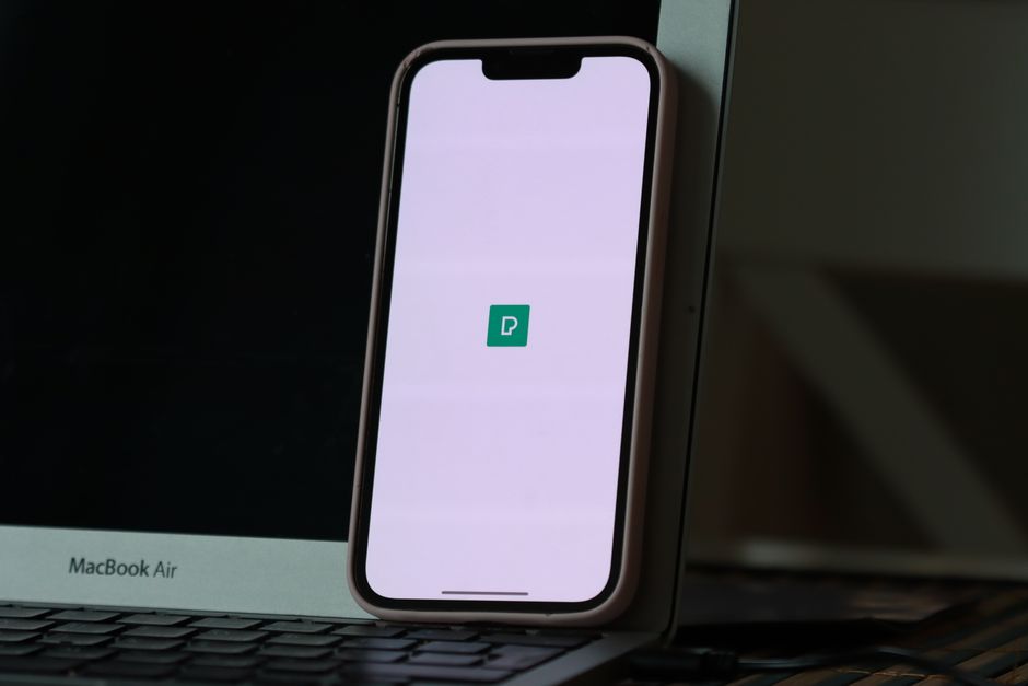 Smartphone resting against a laptop screen with app icon displayed, indoors.