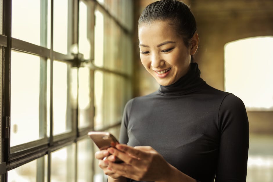 Happy woman in black turtleneck uses smartphone by a sunlit window indoors.